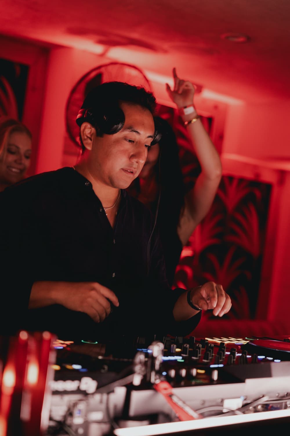 LP behind the decks in red light, headphones around his neck