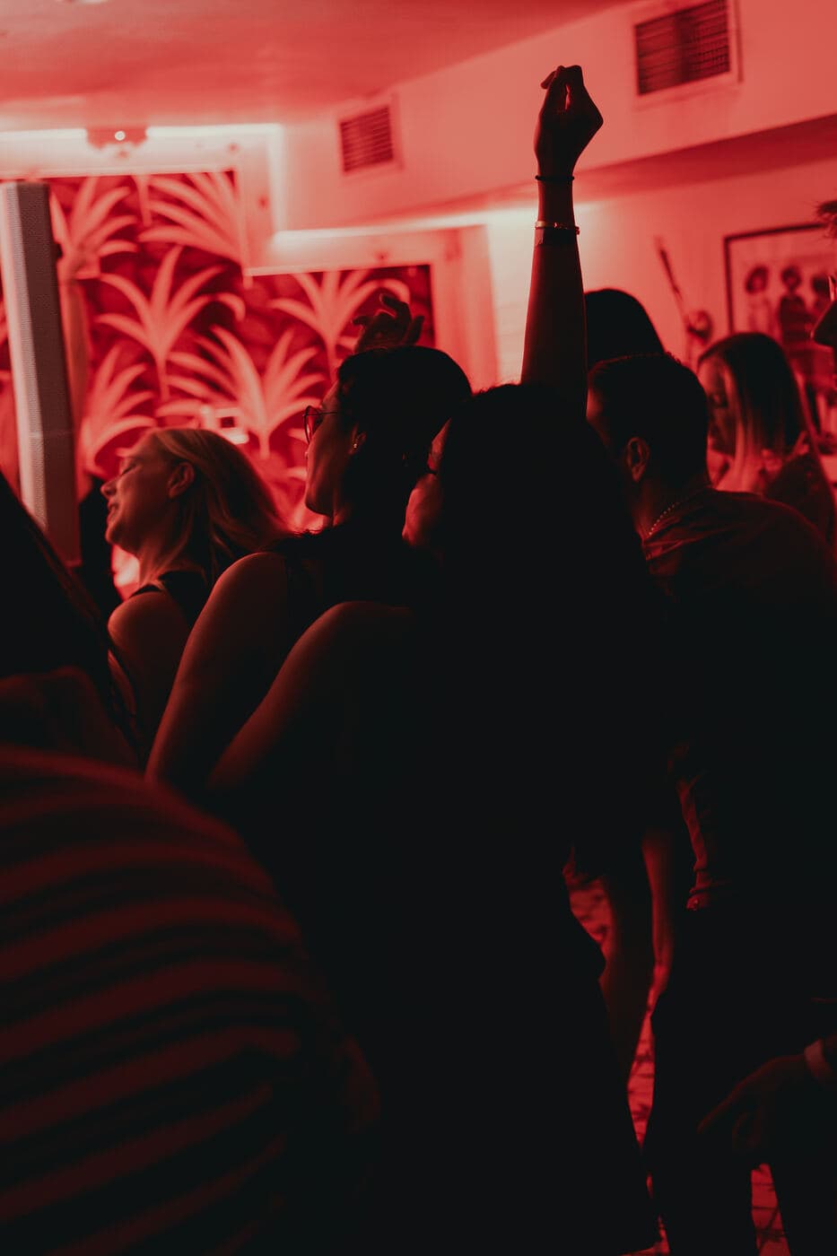 Silhouetted crowd with hands raised under red light at Mirage