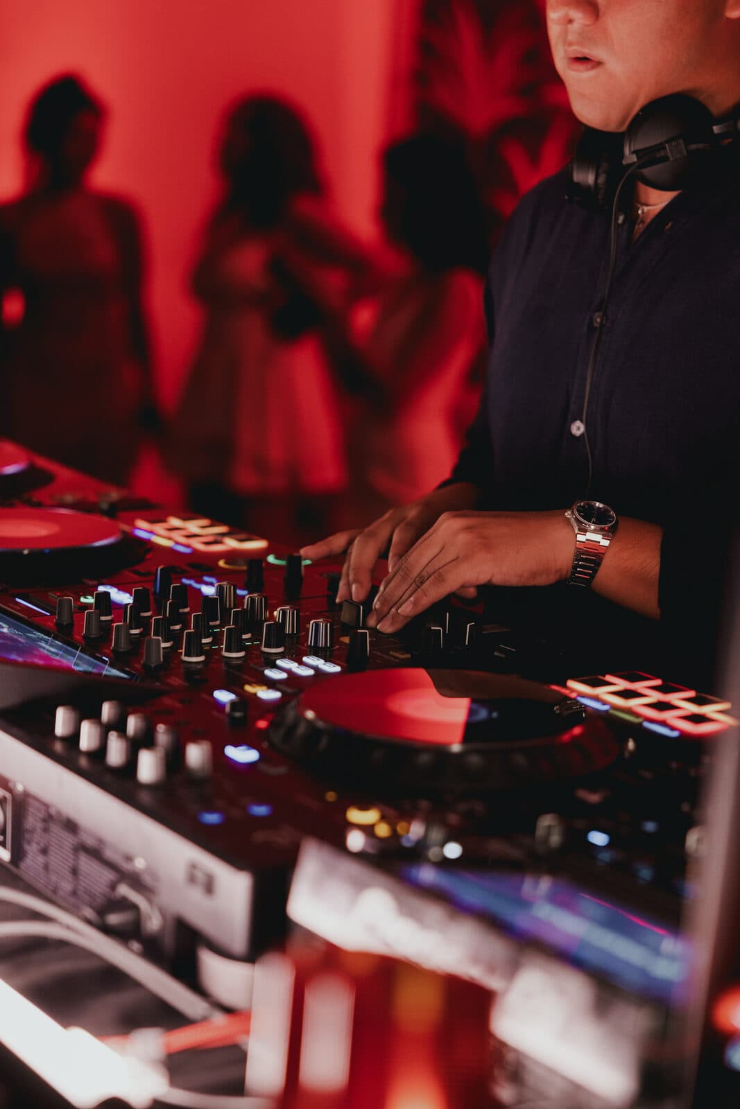 LP behind the decks, close on his hands working the mixer, lit in red